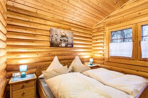 Quarto de cabana de toras com cama, mesas de cabeceira, abajur e um quadro na parede.