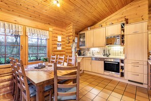 A log cabin interior with a wooden dining table, chairs, a kitchen with wooden cabinets, a microwave, and a stove. - Holiday Home 'Hohlwegstübchen' with Shared Terrace, Shared Garden and Wi-Fi (Sundern (Sauerland))