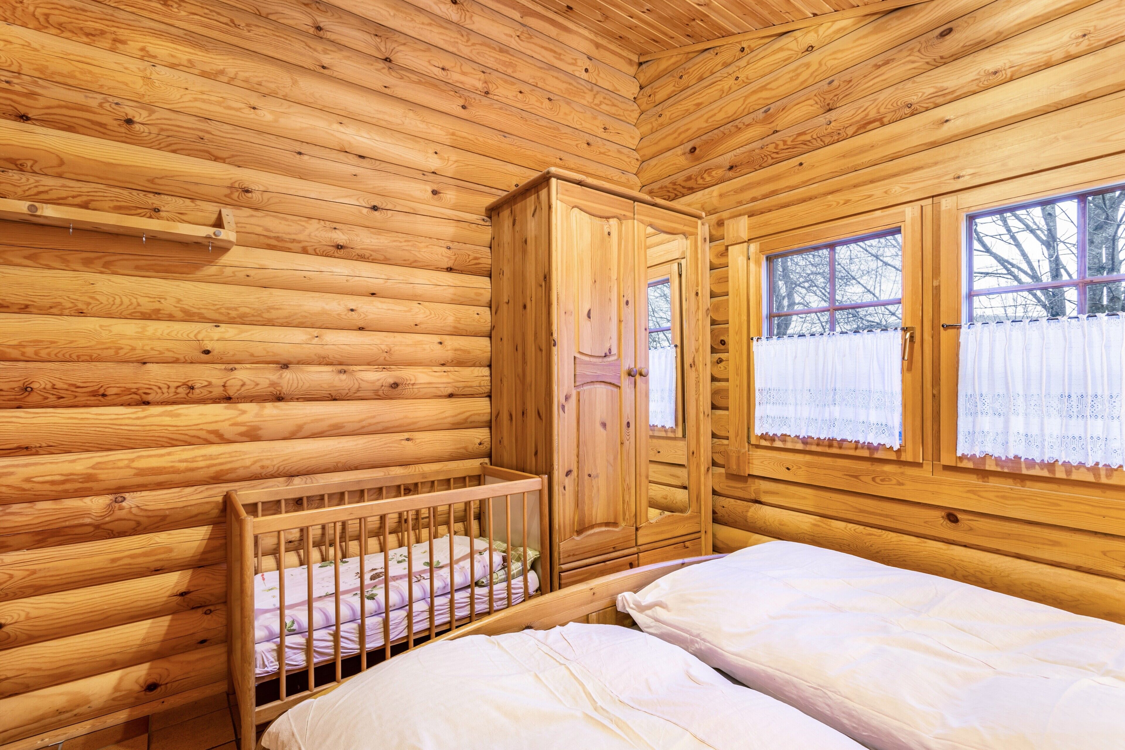 Een houten kamer met een ledikantje, een bed en een kledingkast.