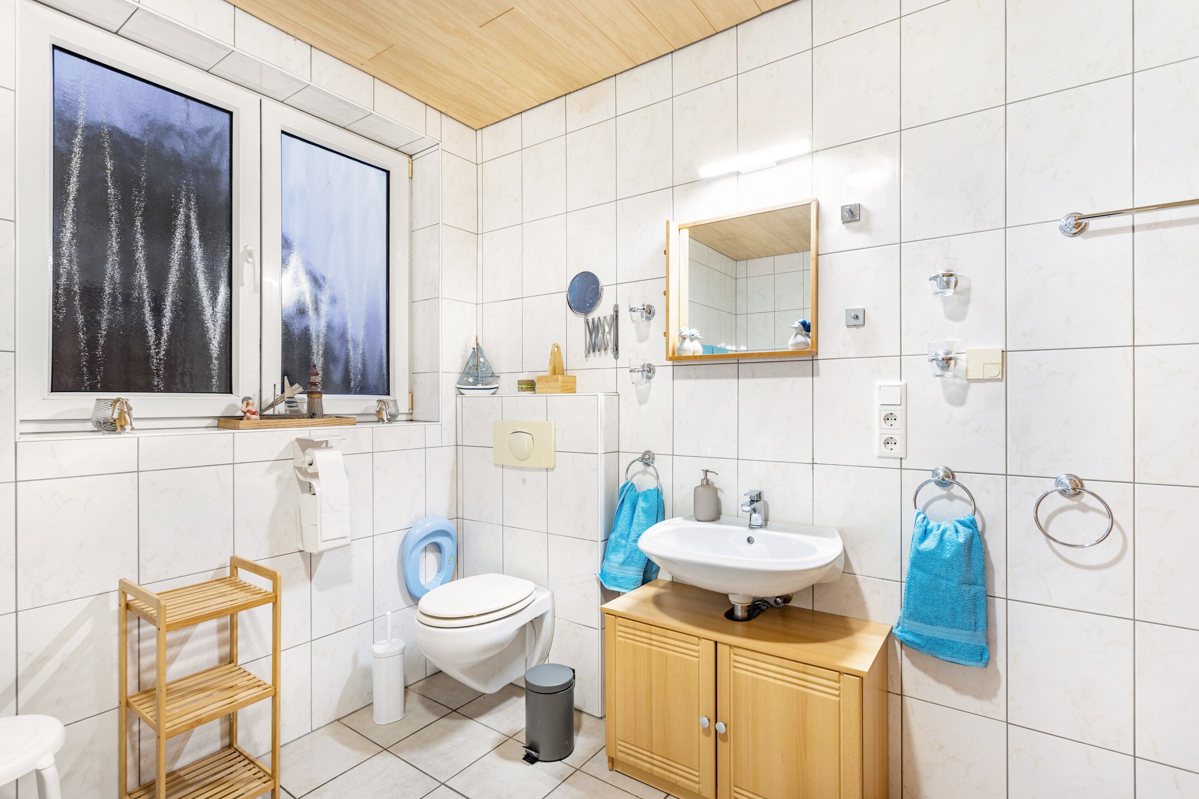 A bathroom with a toilet, sink, mirror, and a window with a view of trees.