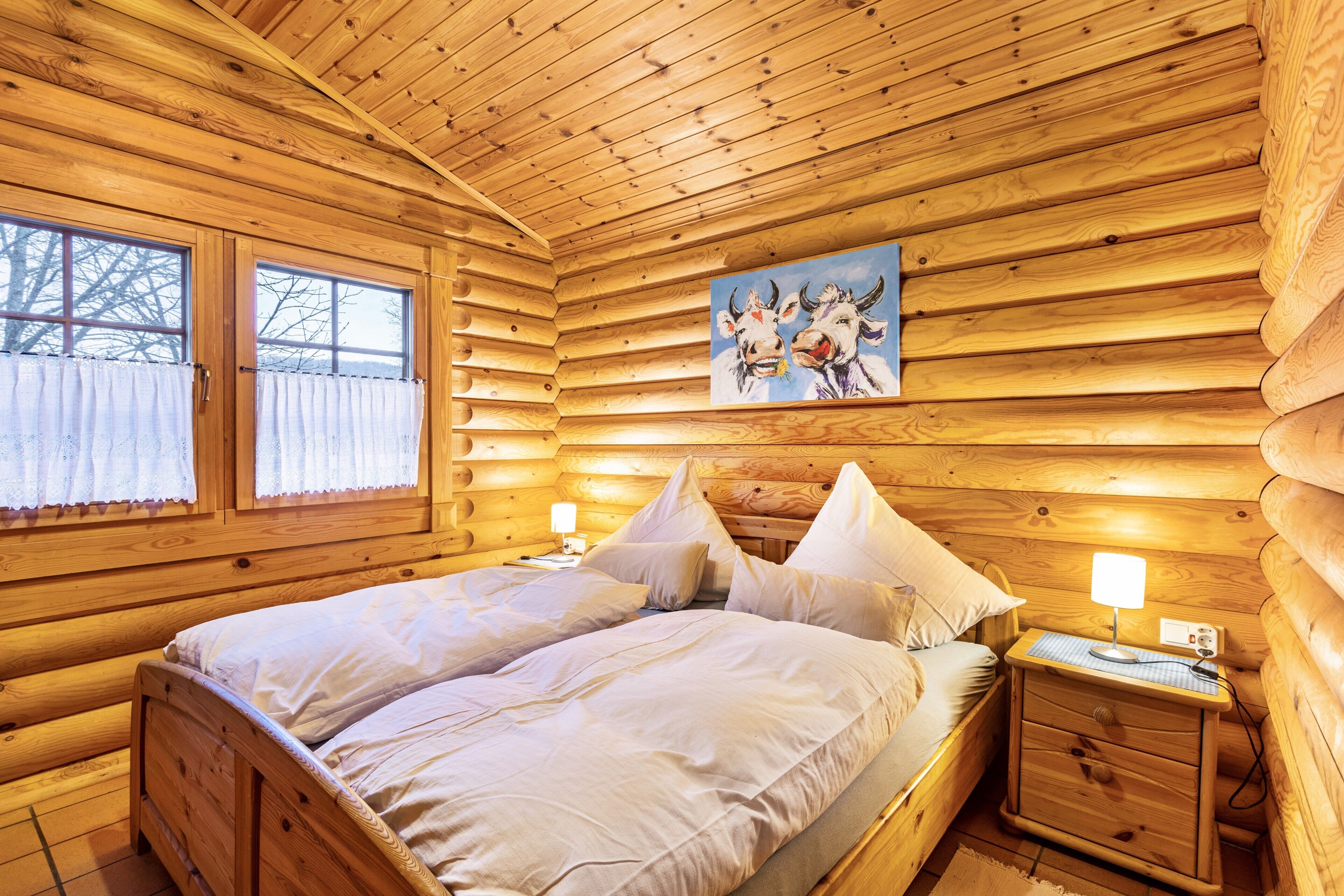 A wooden cabin bedroom with a bed, nightstands, and a painting on the wall.