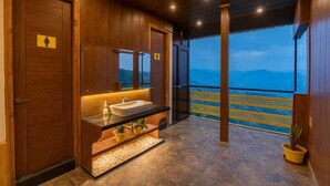 A modern bathroom with wooden walls, a sink, and a mirror. There is a view of mountains through the window. - The Hosteller Kufri, Shimla (Theog)