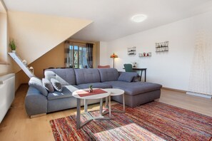 A modern living room with a grey sectional sofa, a small round table, a colorful rug, and a staircase leading to an upper level.
