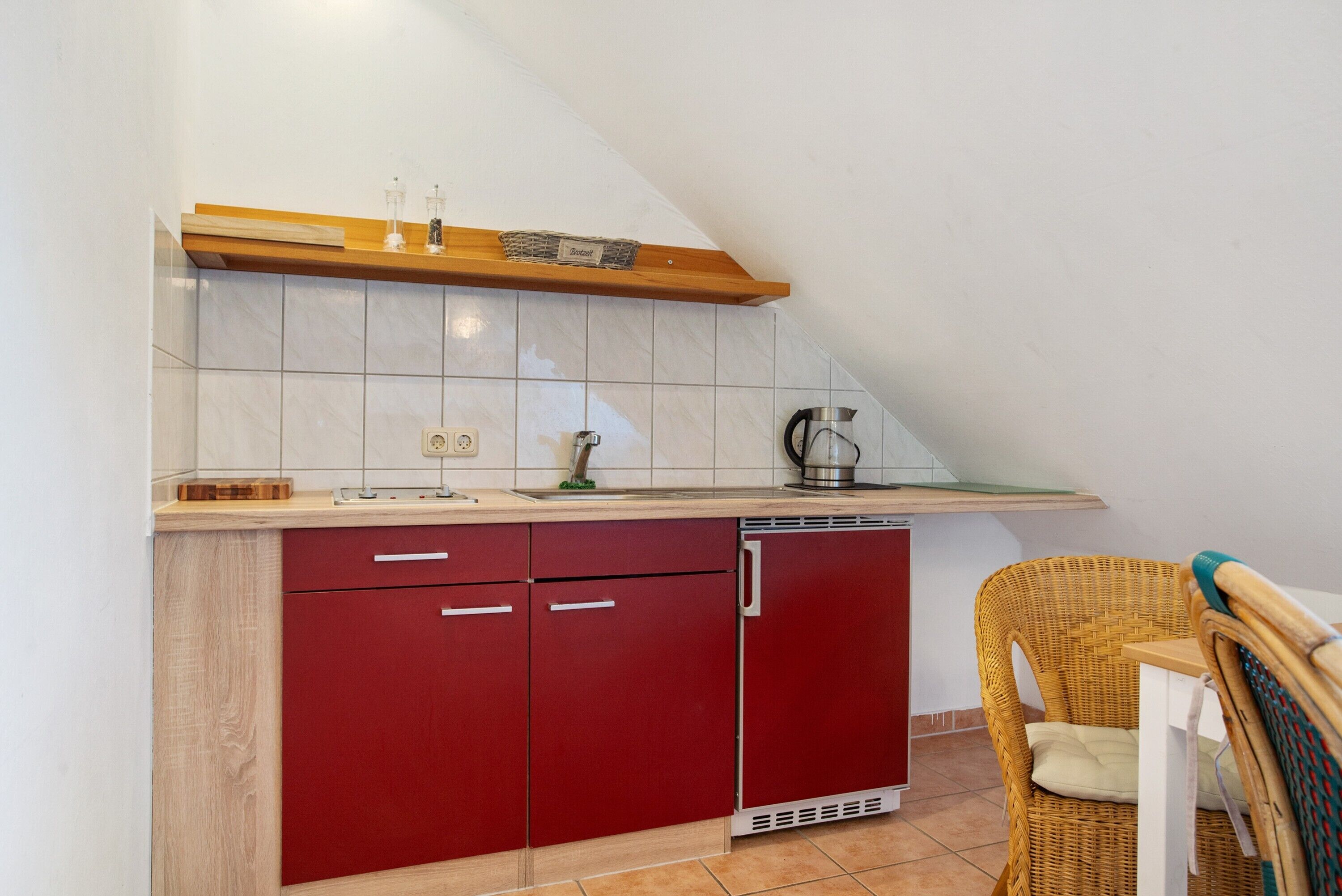 Eine Küche mit einem roten Kühlschrank, einer Holzablage und einem Korbstuhl.