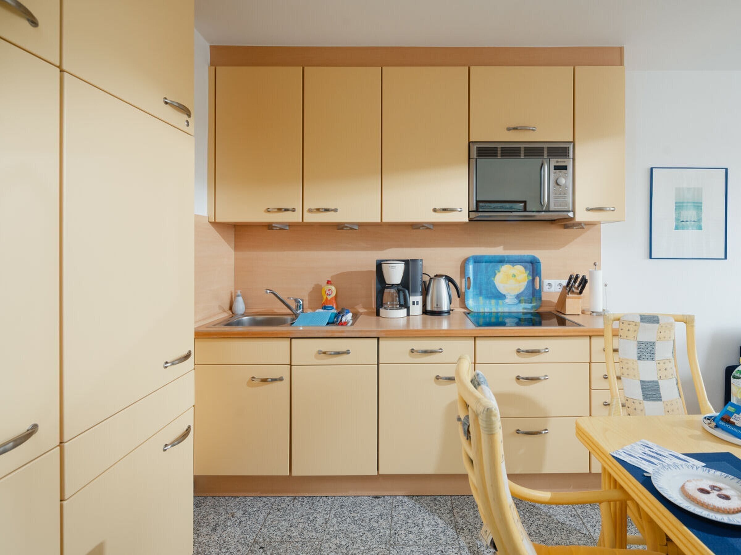 Een kleine keuken met een magnetron, koffiezetapparaat en een blauw snijplank.