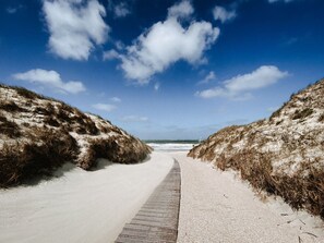 Een pad dat naar een strand leidt, met duinen aan beide kanten.