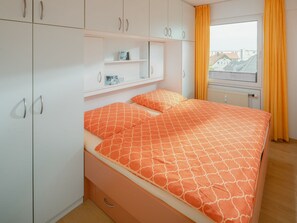 Une chambre à coucher avec un lit, une armoire, une étagère et une fenêtre avec des rideaux.