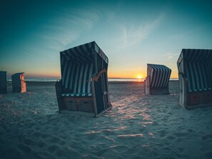 Sillas de playa con toldos a rayas en una playa arenosa al atardecer.