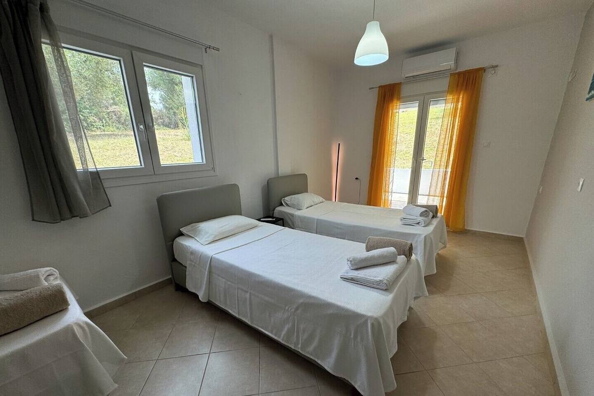 Habitación de hotel con dos camas individuales, un escritorio pequeño, una silla, ventana con cortinas y un equipo de aire acondicionado.