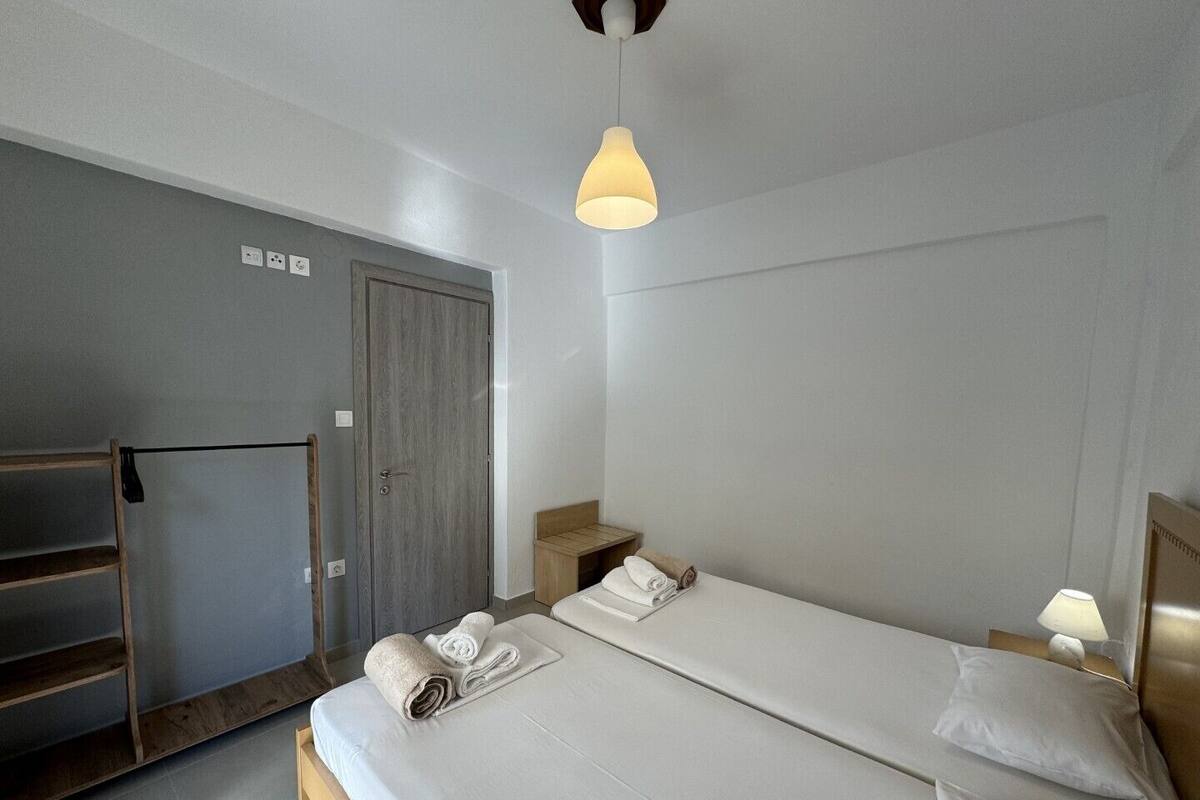 Una habitación de hotel con dos camas, un armario de madera, un banco y una lámpara colgante.