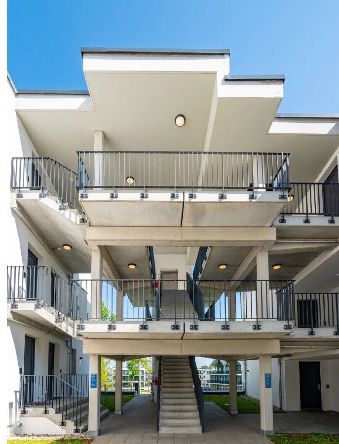 A multi-story building with balconies, a central staircase, and a covered entrance area.