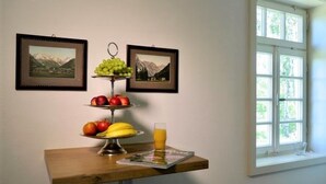 Taula amb un arranjament de fruita, un got de suc i dues fotografies emmarcades a la paret.