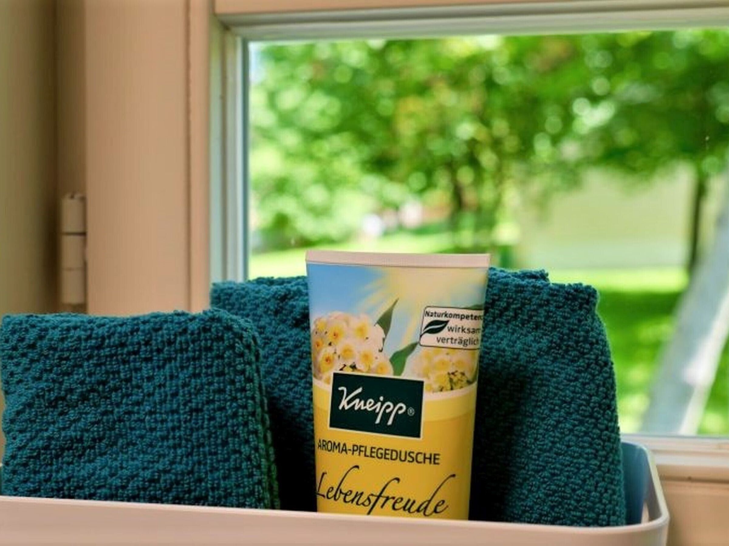 Ein Fenster mit Blick auf Grünflächen, ein blau gestricktes Accessoire und eine Tube Kneipp Aromatherapieöl.