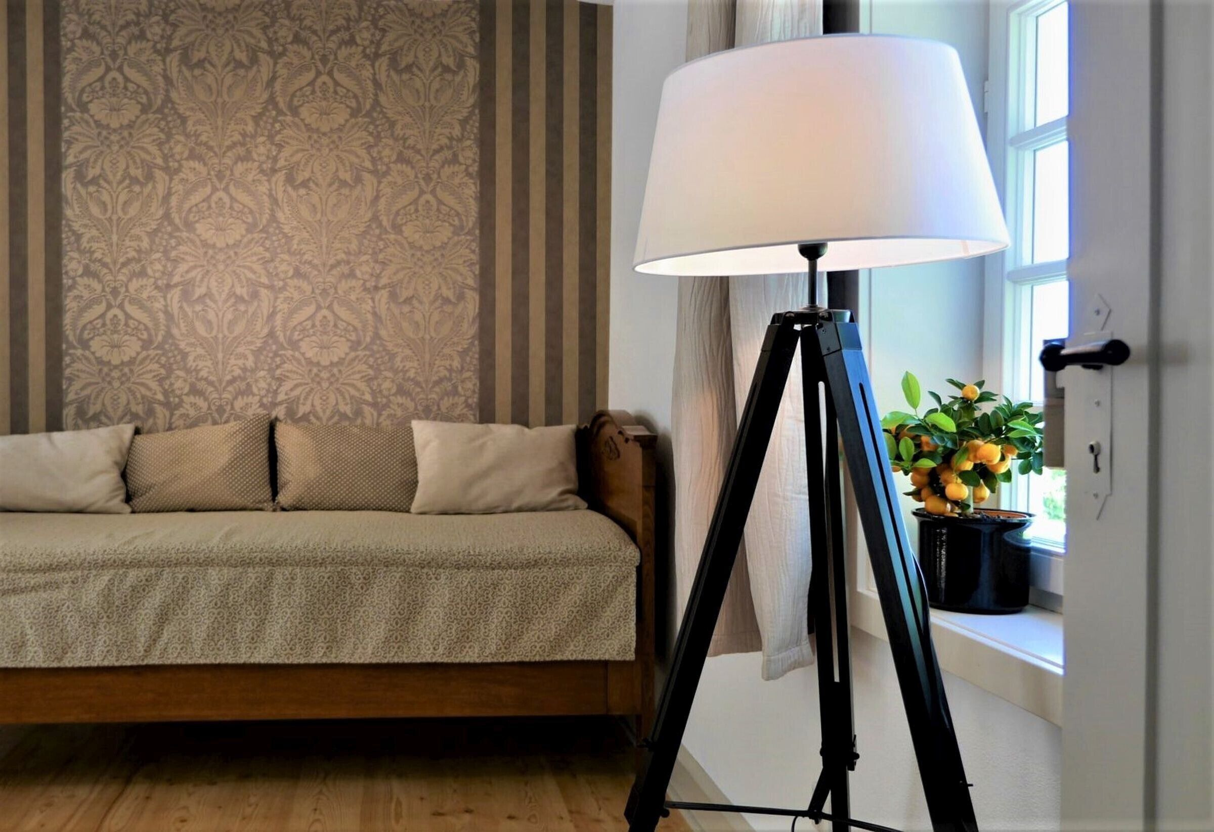 Ein Zimmer mit einer Couch, einer Stehlampe und einem Fenster mit Pflanze.