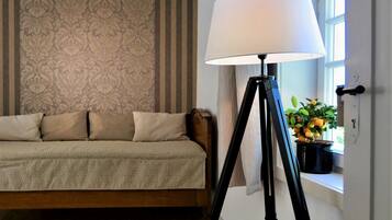 Ein Zimmer mit einer Couch, einer Stehlampe und einem Fenster mit Pflanze.