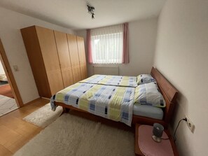 Une chambre à coucher comprenant un lit, une armoire, une fenêtre avec des rideaux et une table de chevet avec une lampe.