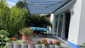 A patio with a table and chairs, a blue awning, and a variety of potted plants and flowers. - Waibel Apartment, 60 sqm, 1 Bedroom, Terrace, Sleeps up to 3 Guests (Überlingen)