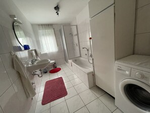 A bathroom with a sink, toilet, shower, and a washing machine.