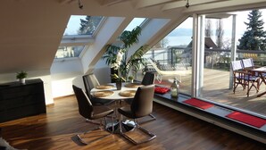 A dining area with a table set for four, a potted plant, and a view of the outdoors through large windows. - Apartment 'Bodenseeblick' with Lake View, Balcony and Wi-Fi (Nonnenhorn)