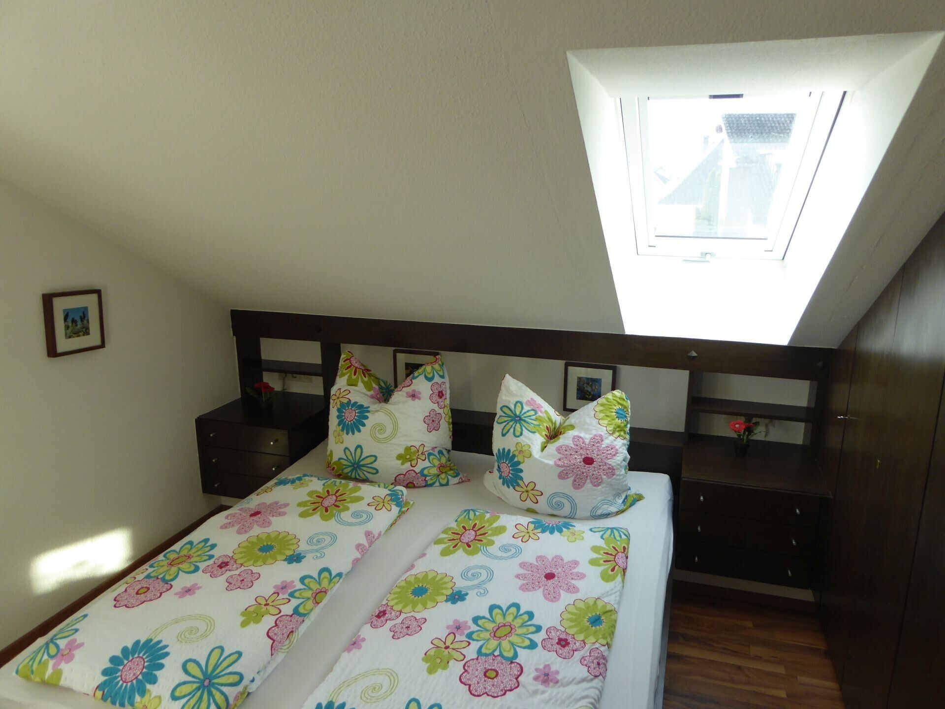 Een slaapkamer met dakraam, een bed met bloemenbedrukking, een nachtkastje en een kledingkast.