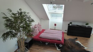 A bedroom with a skylight, a bed with striped bedding, a potted plant, a black dresser, and a cowhide rug. - Apartment 'Bodenseeblick' with Lake View, Balcony and Wi-Fi (Nonnenhorn)