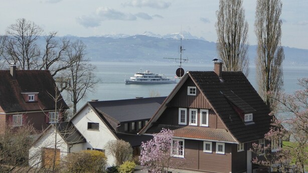 A residential area with houses, a river, and mountains in the background. - Apartment 'Bodenseeblick' with Lake View, Balcony and Wi-Fi (Nonnenhorn)