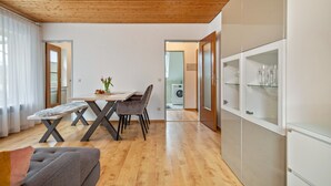 Een moderne woonkamer met een houten plafond, een eettafel met stoelen, een bank en een kast met glazen deuren.