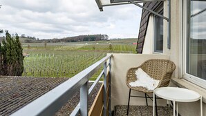 Een balkon met uitzicht op een wijngaard, een rieten stoel en een tafeltje.
