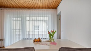 Een eetgedeelte met een tafel, stoelen, een vaas met bloemen en een schaal fruit.