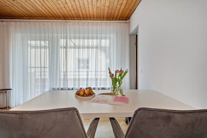 Un coin repas comprenant une table, des chaises, un vase avec des fleurs et un saladier rempli de fruits.