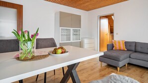 Een moderne woonkamer met een witte eettafel, een grijze bank en een houten plafond.