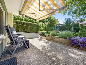 A patio area with a covered seating area, a concrete planter with flowers, and a hedge.