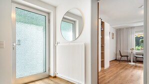 Un intérieur moderne avec une porte vitrée, un radiateur blanc, un miroir rond et un coin repas comprenant une table et des chaises.