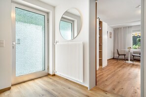 A modern interior with a glass door, a white radiator, a round mirror, and a dining area with a table and chairs.