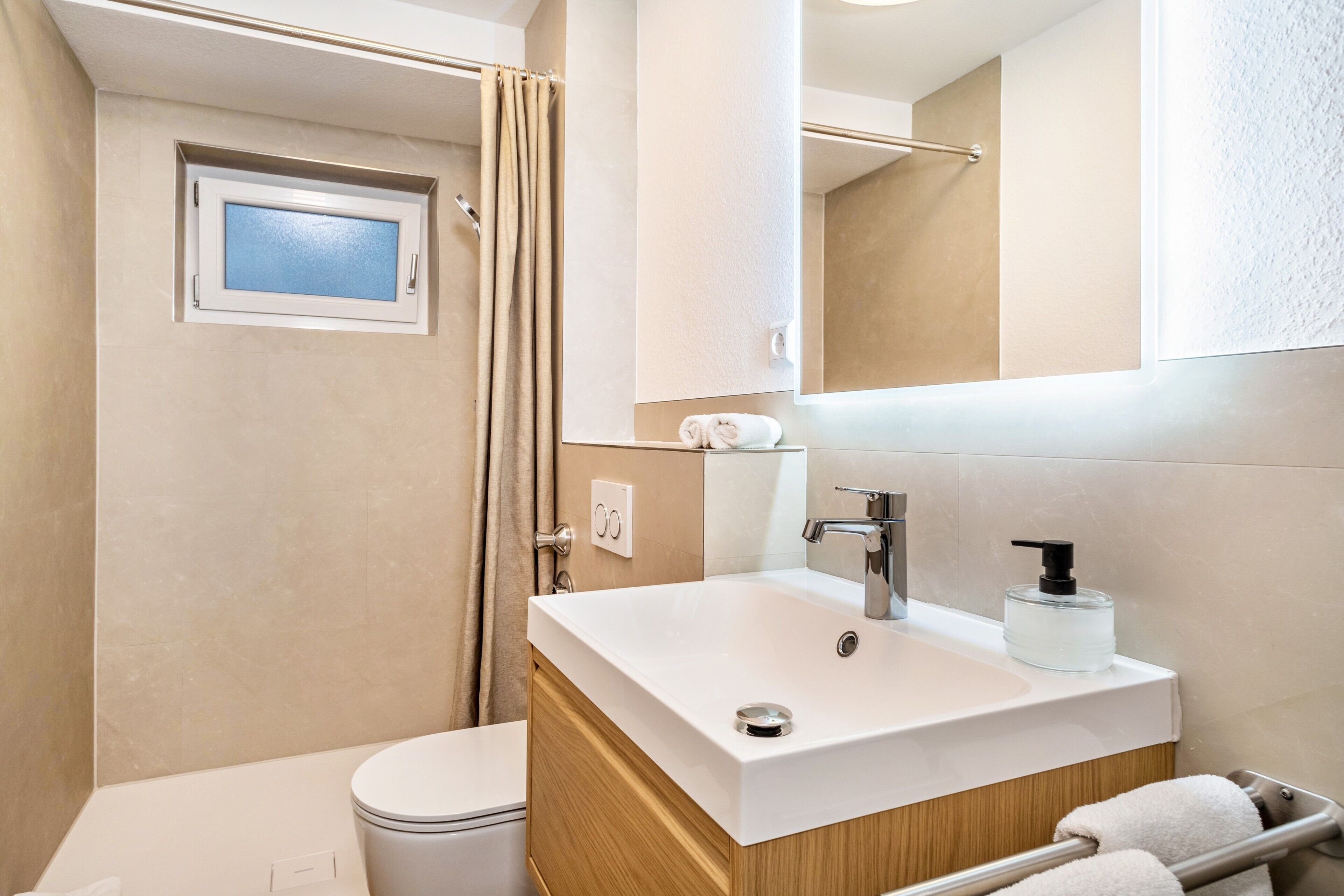A bathroom with a toilet, a sink with a mirror, a shower curtain, and a towel rack.