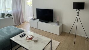 Una sala de estar moderna con una televisión de pantalla plana sobre un mueble blanco, una lámpara de pie y un sofá.