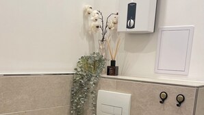 Un baño moderno con inodoro blanco, secamanos de pared y una pequeña planta.