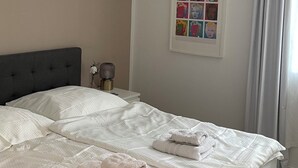 Una cama bien hecha con toallas dobladas, una obra de arte enmarcada en la pared y una ventana con cortinas.