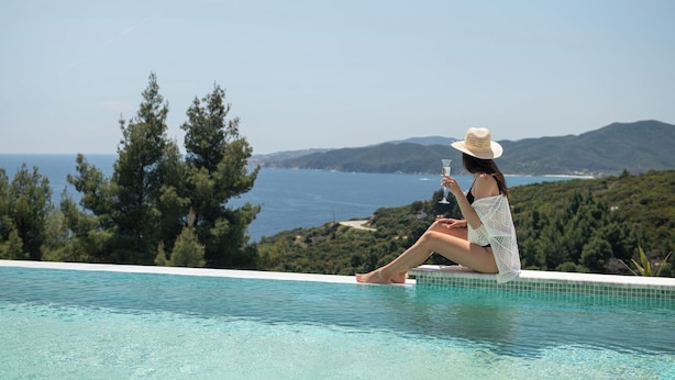 Una mujer sentada junto a una piscina con vista al mar y colinas.