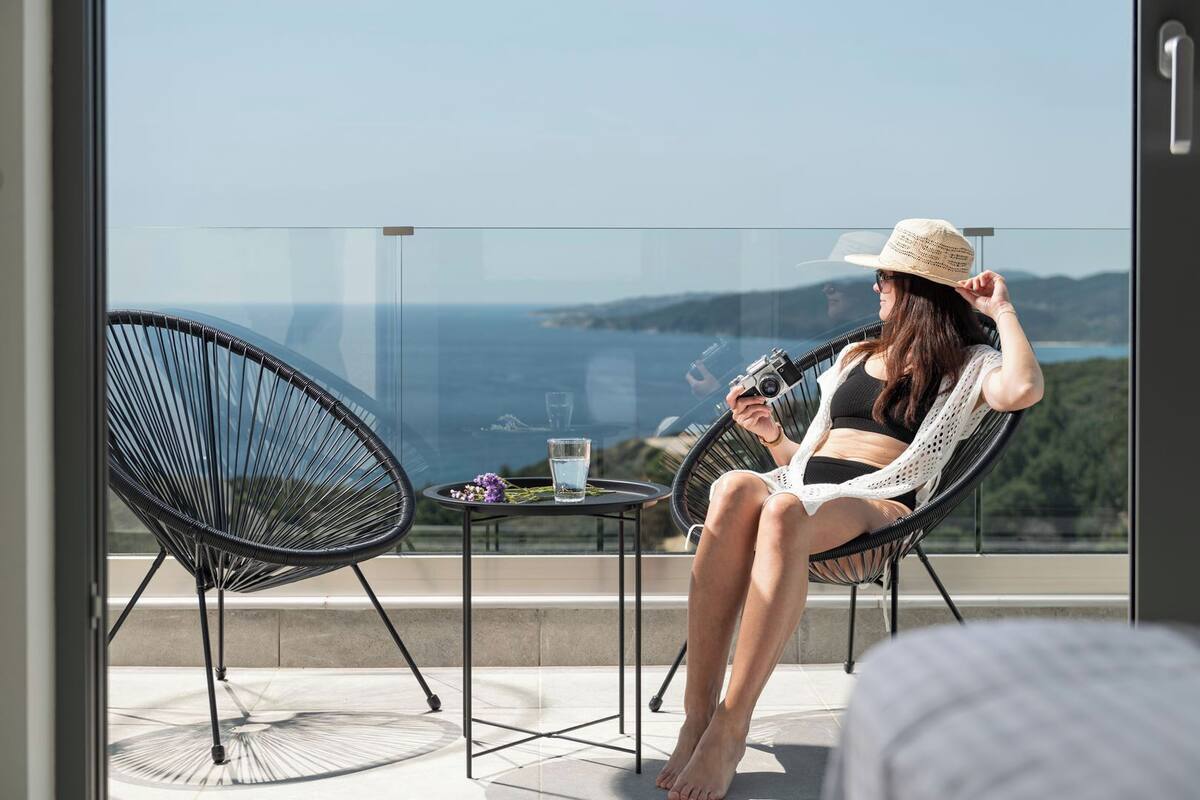 A person sitting on a chair on a balcony with a view of the sea.
