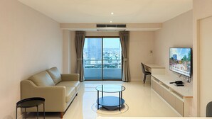 A modern living room with a sofa, a coffee table, a TV, and a view of the city. - Avana Residence (Bangkok)
