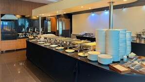 A buffet setup with various food stations and stacked plates. - Avana Residence (Bangkok)