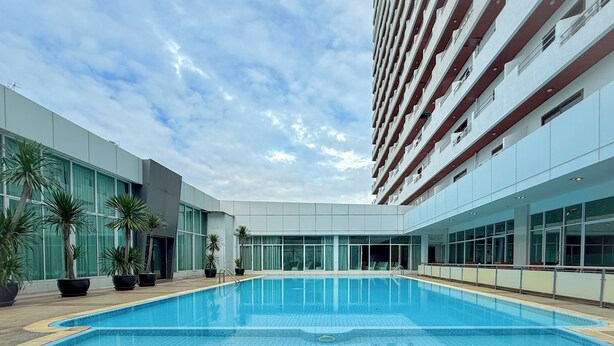 A modern hotel with a central swimming pool, large windows, and potted plants. - Avana Residence (Bangkok)