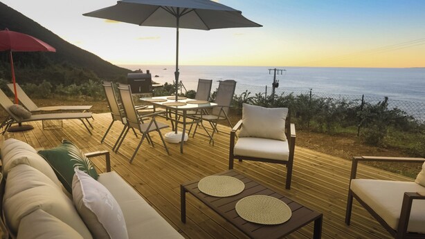 Terraza con mesa y sillas, un sofá y una sombrilla, con vista a un cuerpo de agua.