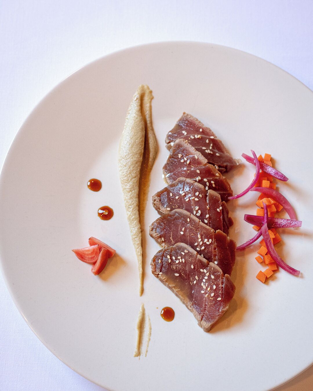 A plate with sliced meat, sesame seeds, and vegetables.