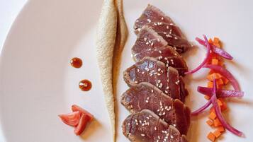 A plate with sliced meat, sesame seeds, and vegetables.