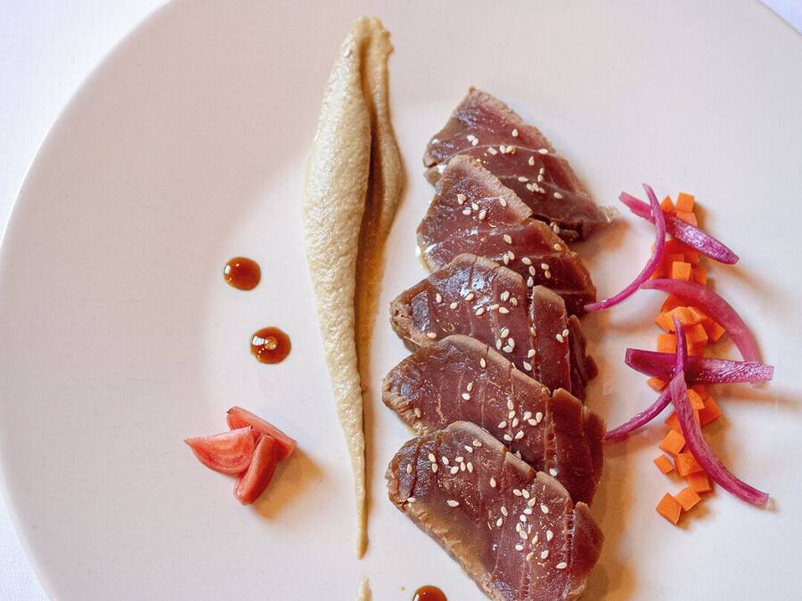 A plate with sliced meat, sesame seeds, and vegetables.