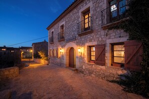 A stone building with arched doorways and wooden shutters, illuminated by warm lighting. - La Siuranella (Siurana)
