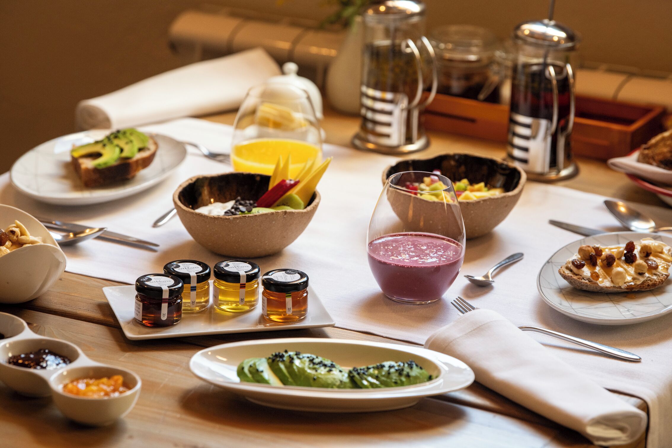 A breakfast setting with various dishes, including toast with avocado, a bowl of fruit, and a glass of smoothie.