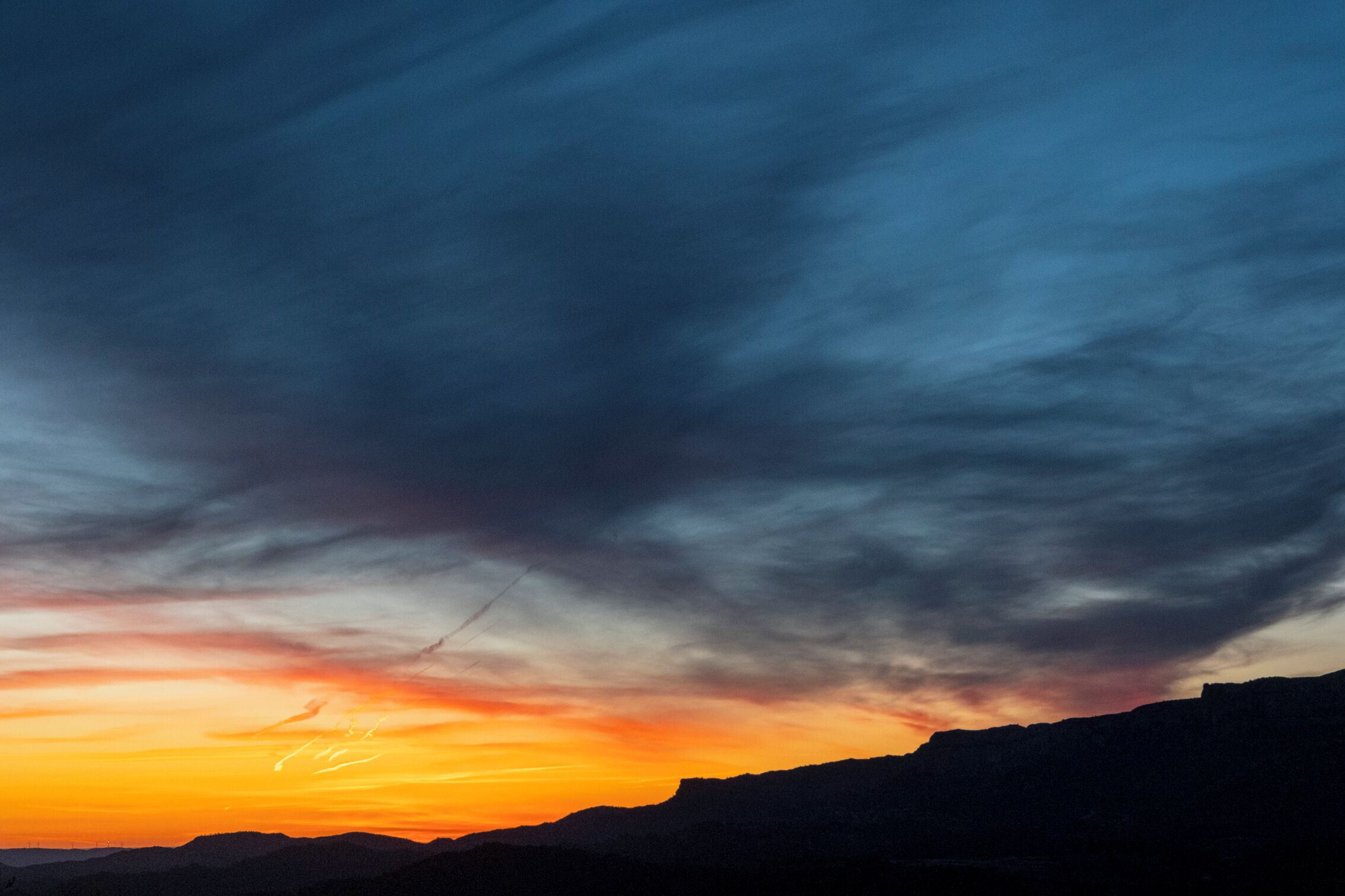 Een zonsondergang boven een bergachtig landschap met een heldere lucht.